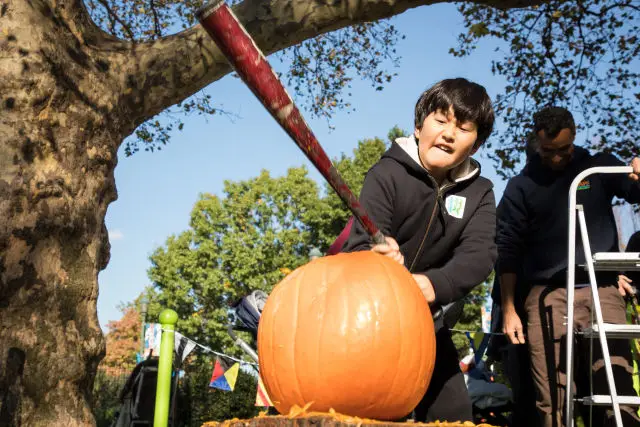 A low-angle shot of a boy ready to fling a pumpkin from a slingshot at a Pumpkin Smash event.